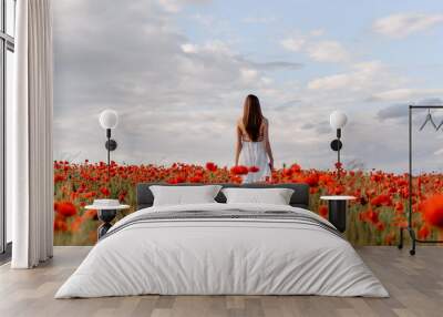 Back view of a woman in white dress walking in a red poppies field Wall mural