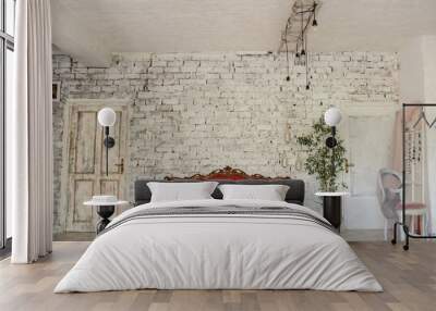 Closeup photo of a red vintage sofa on a white and brown brick wall sorrounded by plants, candles, a chair with a pink curtain on it in a light and large room Wall mural