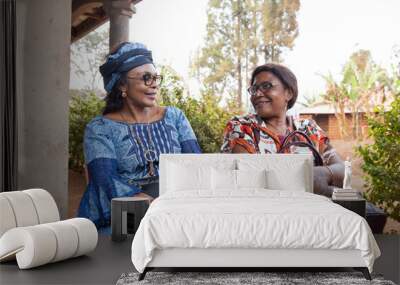 Two senior African ladies friends are sitting and chatting, African women traditionally dressed together, adult friendship concept Wall mural