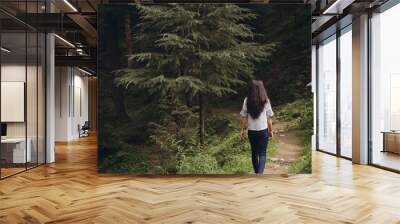 Back view of a young brunette Indian girl walking through the forest full of lush green trees Wall mural