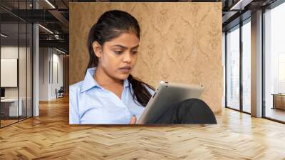 Indian female using a tablet sitting on the couch Wall mural