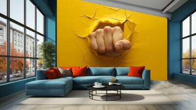 A hand is punching through a yellow wall. Concept of power and strength, as the hand is able to break through the wall Wall mural