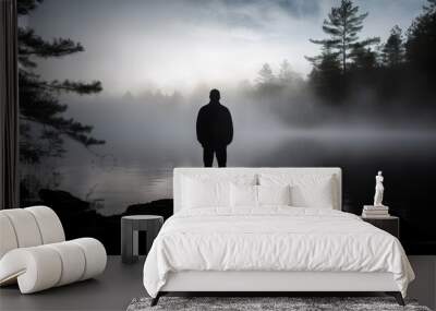 A man stands on a lake in the fog. The scene is quiet and peaceful, with the man being the only person in the image. The fog adds a sense of mystery and solitude to the scene Wall mural