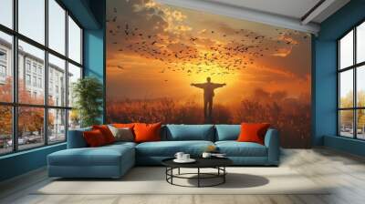 A person is standing on the beach with his arms outstretched, surrounded by a flock of birds. The scene is serene and peaceful, with the man and birds both enjoying the beauty of the sunset Wall mural