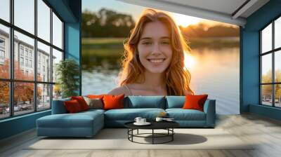 Teenager with a carefree smile, standing by a lake with the sun setting behind Wall mural