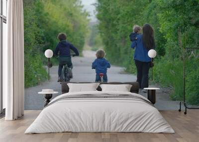 Two children riding bicycles, mother holding baby and walk on empty forest road Wall mural