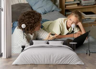 Mother talking to her daughter while they lying on bed and using laptop in bedroom Wall mural