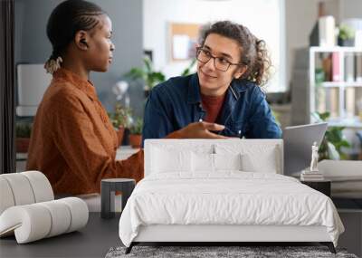 Portrait of smiling young man with long hair listening to female colleague discussing ideas during meeting at workplace in office Wall mural