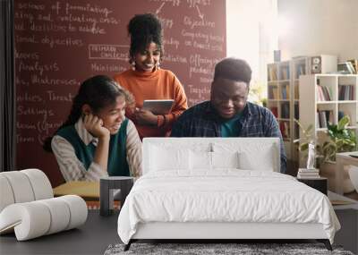 Portrait of three Black college students looking at laptop screen in class and smiling cheerfully Wall mural