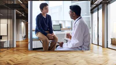 Portrait of young boy listening to doctor while sitting on cot in medical clinic copy space Wall mural