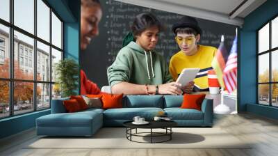 Two teenage girls collaborating on project and using digital tablet while sitting at table during lesson in school classroom Wall mural