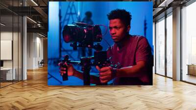 Young African American camera operator shooting on professional camera in dark studio Wall mural