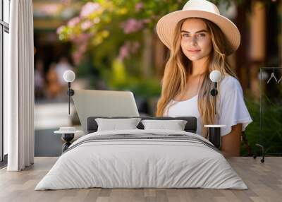 A woman wearing a straw hat is sitting in front of a laptop Wall mural