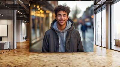 A young man wearing a hoodie and jacket is smiling for the camera Wall mural