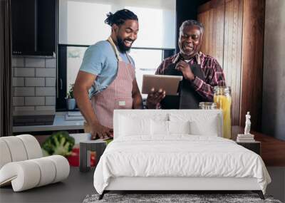 Adult son with his senior father cooking in the kitchen. Wall mural