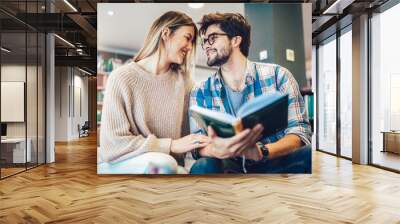 Attractive young couple in a library reading a book together Wall mural