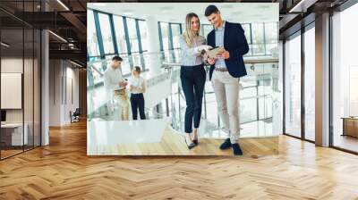 Beautiful business woman and man holding a tablet in their hands and smiling. In the background are business people. Wall mural