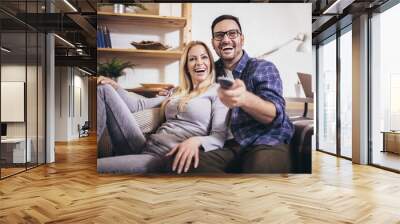 Cheerful couple is watching tv together and having fun in the living room. Wall mural