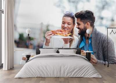 Couple eating pizza outdoors and smiling.They are sharing pizza in a outdoor cafe. Wall mural