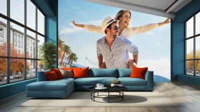 Couple in love, enjoying the summer time by the sea.Joyful girl piggybacking on young boyfriend having fun. Wall mural