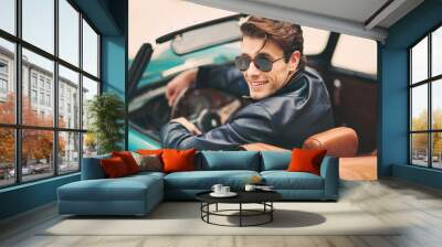 Fashion man sitting in luxury retro cabriolet car outdoors Wall mural