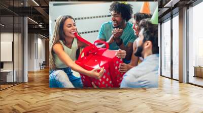 Friends celebrating birthday and giving gift to a girl at home party Wall mural