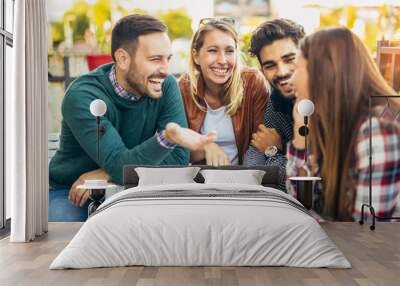 group of four friends having fun a coffee together. two women and two men at cafe talking laughing a Wall mural