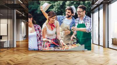 Group of friends stand at a barbecue, one cooking at grill Wall mural