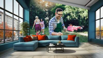 Handsome male preparing barbecue outdoors for friends Wall mural