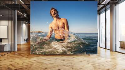 Handsome young man posing on the beach by the sea Wall mural