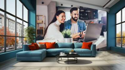 Happy couple doing business together working at home on the laptop. Wall mural