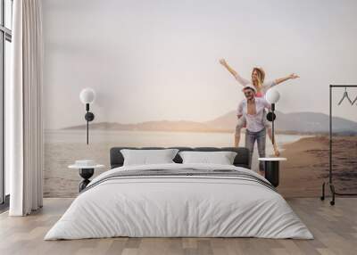 Happy couple in love on beach summer vacations. Joyful girl piggybacking on young boyfriend having fun. Wall mural