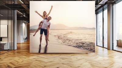 Happy couple in love on beach summer vacations. Joyful girl piggybacking on young boyfriend having fun. Wall mural