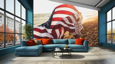 Happy young girl friends enjoys a sunny day on the beach. They're holding an american flag. Wall mural