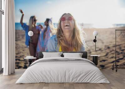 Happy young woman on the beach with her friends in background. Group of friends enjoying on beach holiday. Wall mural