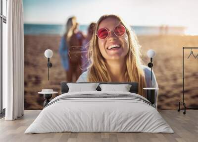 Happy young woman on the beach with her friends in background. Group of friends enjoying on beach holiday. Wall mural