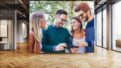 Image of four happy smiling young friends walking outdoors in the park holding digital tablet Wall mural