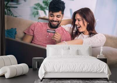 Man using laptop and woman holding credit card. Young couple shopping online with credit card at home Wall mural