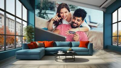 Man using laptop and woman holding credit card. Young couple shopping online with credit card at home Wall mural