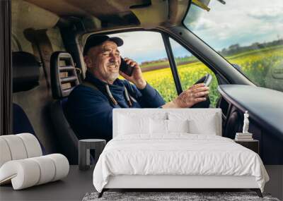 Mature truck driver using mobile phone while driving transport vehicle. Wall mural