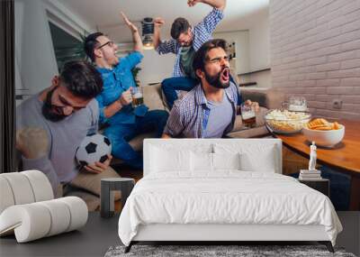 Men watching sport on tv together at home screaming cheerful. Group of friends sitting on the couch and watching a football game. Wall mural