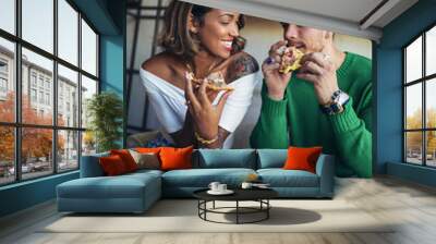 Mixed race couple eating pizza in modern cafe. They are laughing and eating pizza and having a great time. Wall mural