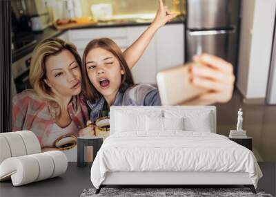 Mother and daughter drink tea or coffee and make selfie with phone. Wall mural