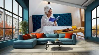 Pretty girl in the hotel room with bathrobe chilling and reading a book. Wall mural