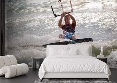 Professional kiter does the difficult trick. A male kiter rides against a beautiful background of waves and performs all sorts of maneuvers. Wall mural