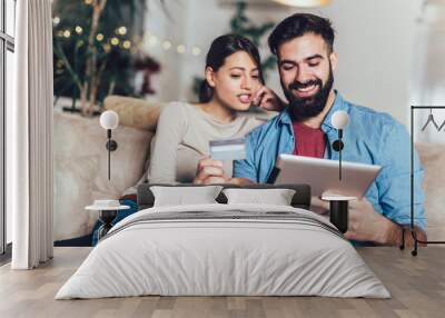 Smiling couple using digital tablet and credit card at home Wall mural