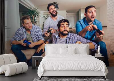 Smiling male friends playing video games at home and having fun. Wall mural