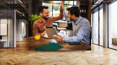 Two colleagues high five in coffee shop. They met to talk about work. Using tablet. Wall mural