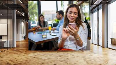 Woman using her phone in the restaurant. Her friends are in the background. Wall mural