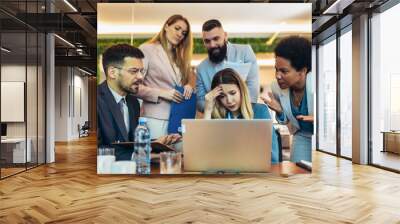 Young businesswoman working on laptop feeling stressed out in a demanding office environment at work Wall mural